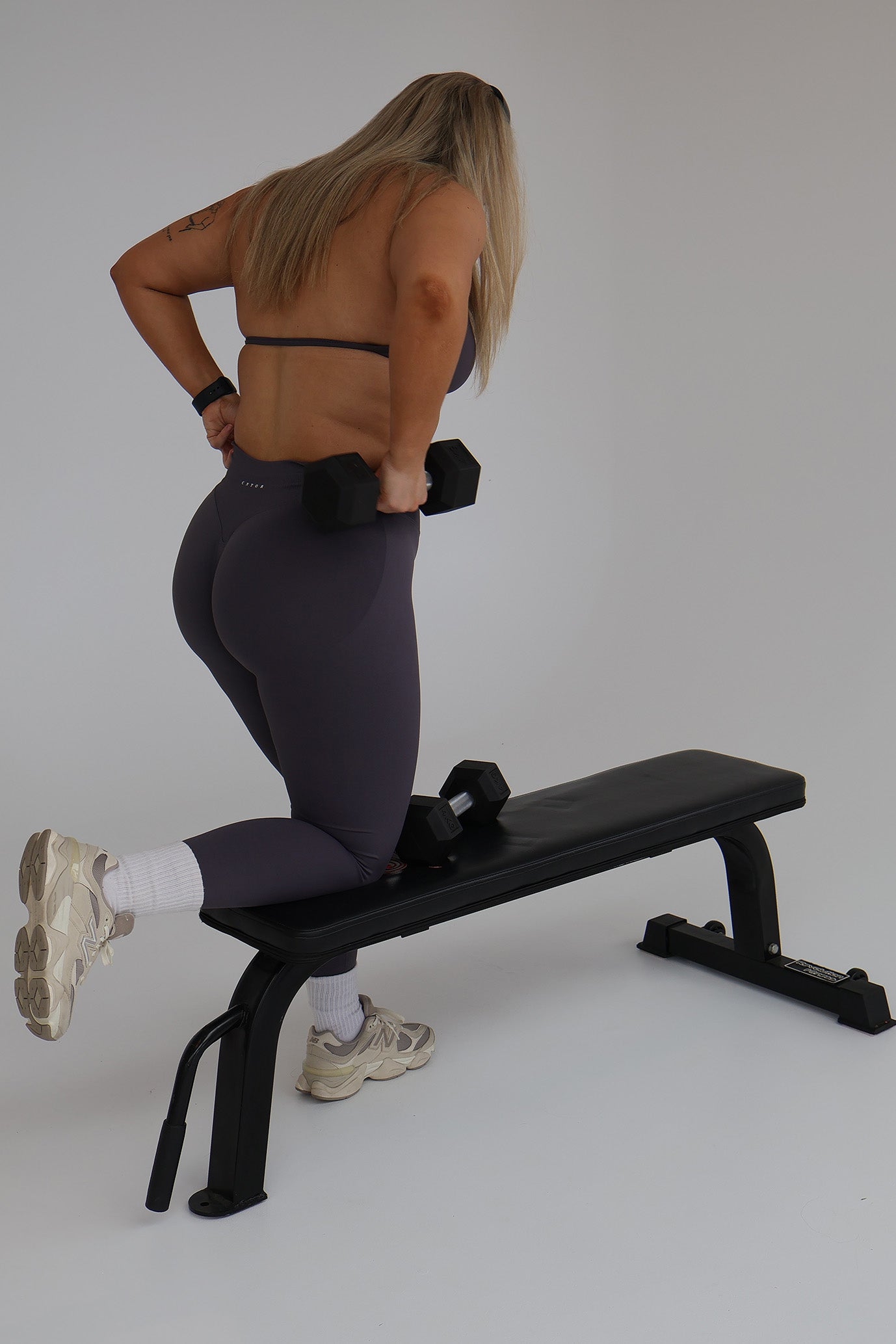 Woman exercising on a weight bench with dumbbells wearing cntor activewear against a plain background