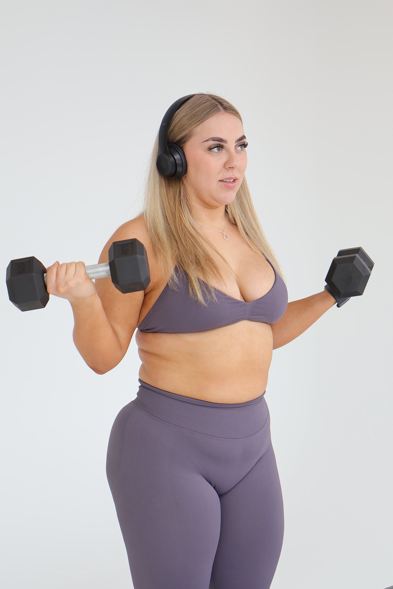 Woman in storm activewear attire with dumbbells and a bench on a plain background