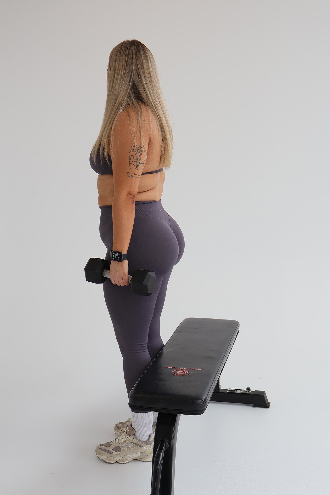 Woman exercising with dumbbells on a weight bench wearing cntor activewear against a plain background
