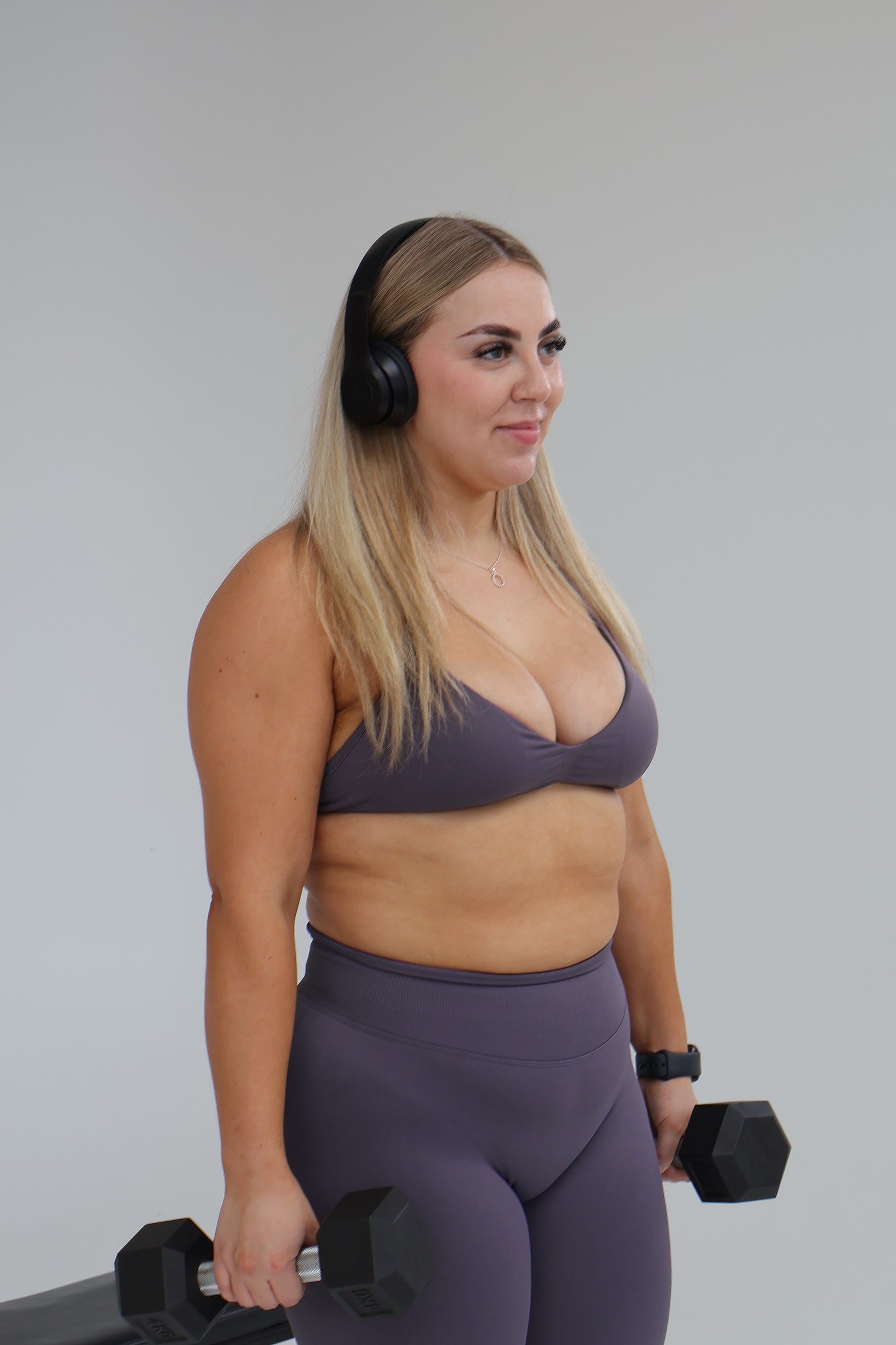 Woman in cntor the label activewear holding dumbbells against a plain background