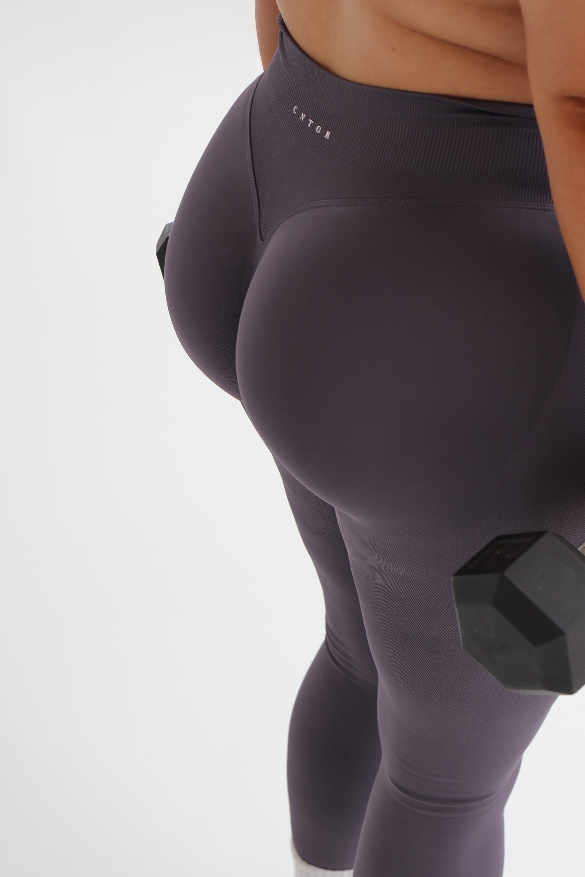 Person wearing cntor the label activewear holding a black dumbbell on a white background